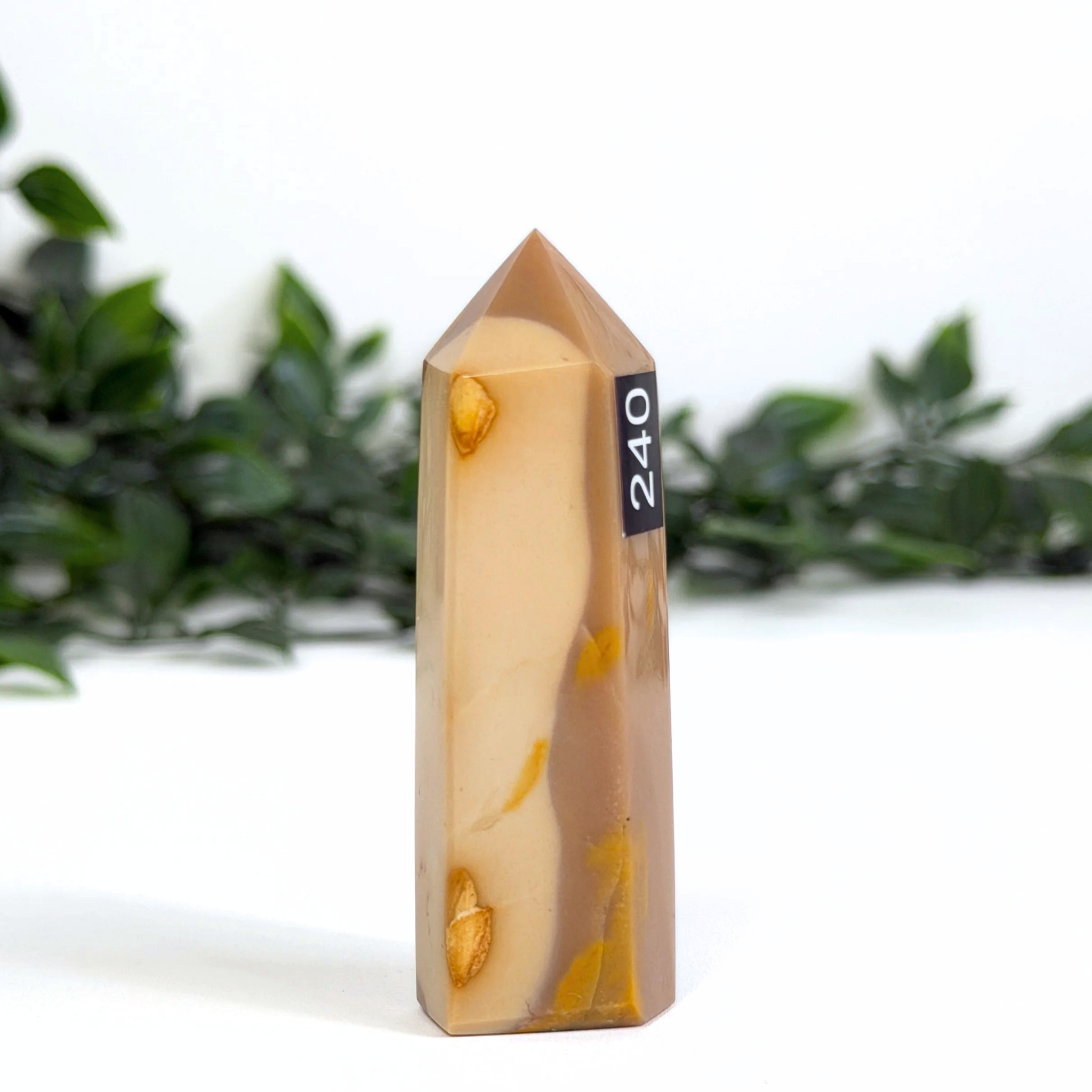 Brown mookaite crystal tower and '240' label against a blurred green foliage background