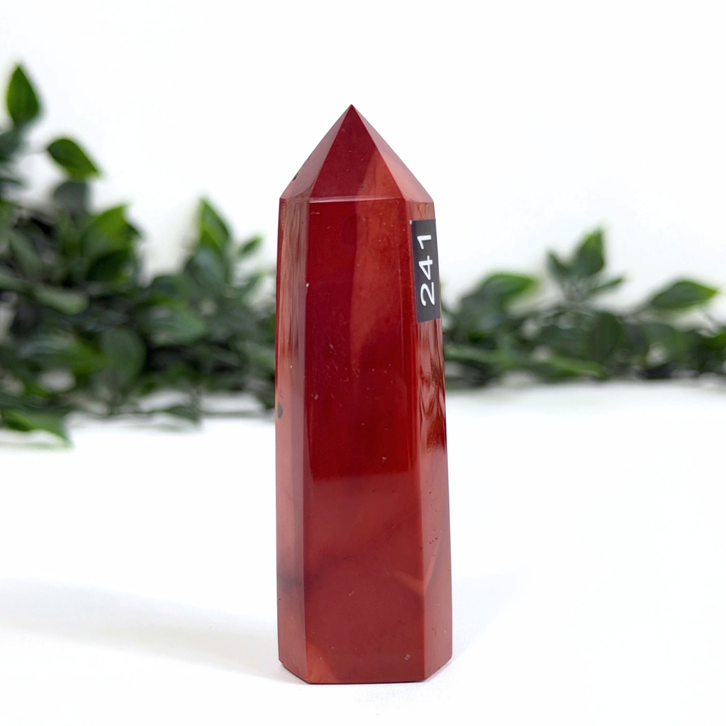 Red mookaite crystal tower with a number tag on a white background with green foliage.