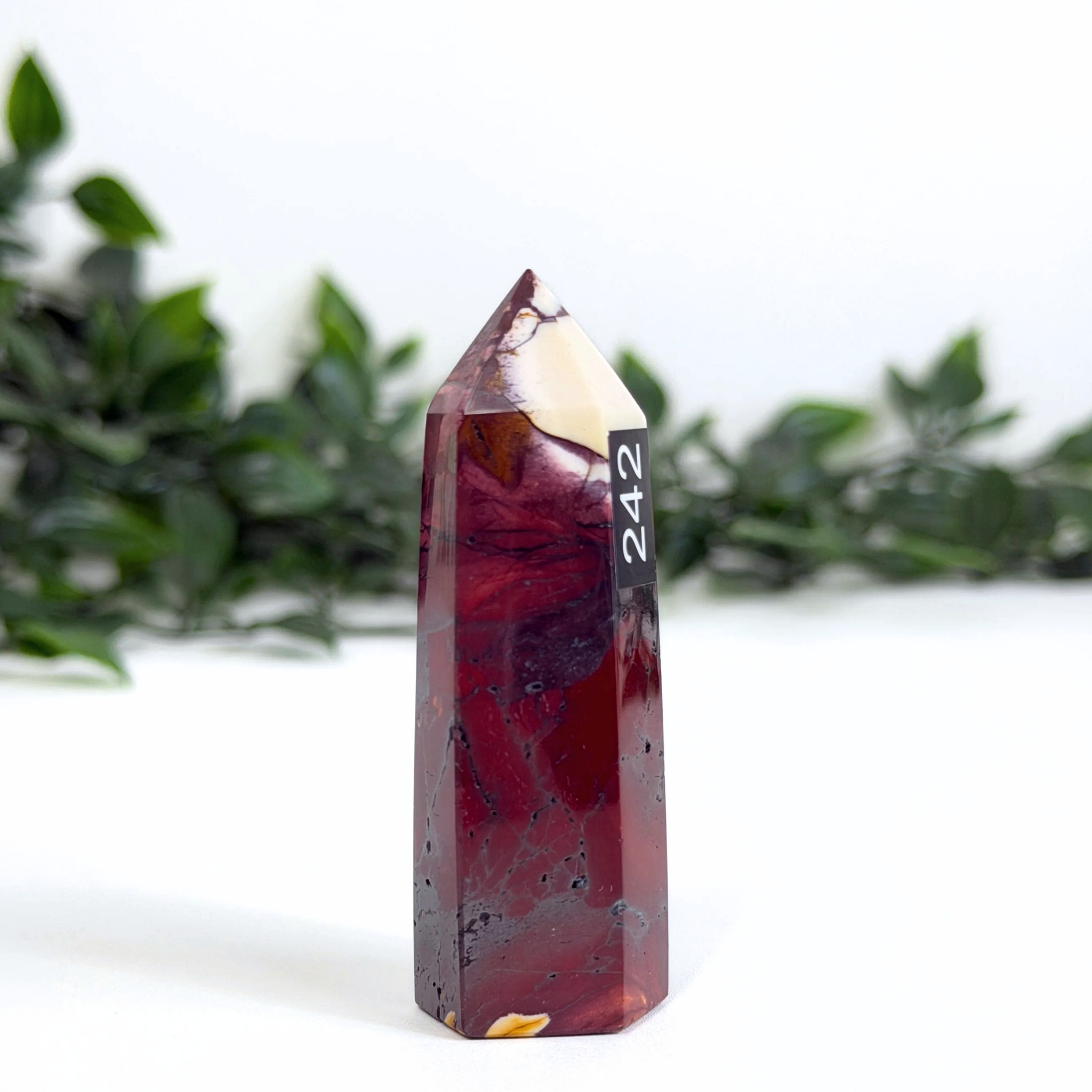 Mookaite crystal tower with '242' marking against a white background with greenery
