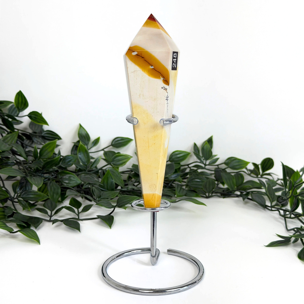 Mookaite crystal wand on a silver stand against a white leafy background.