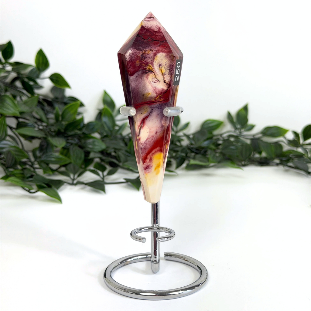 Decorative mookaite crystal wand on a silver stand with a white background and greenery