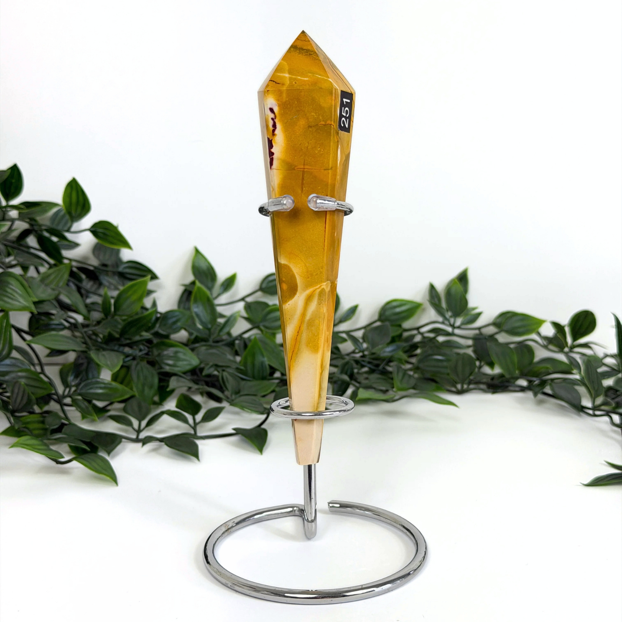 Mookaite crystal wand on a silver stand with green leaves in the background