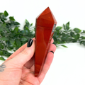 Hand holding a mookaite crystal wand with a blurred green plant background