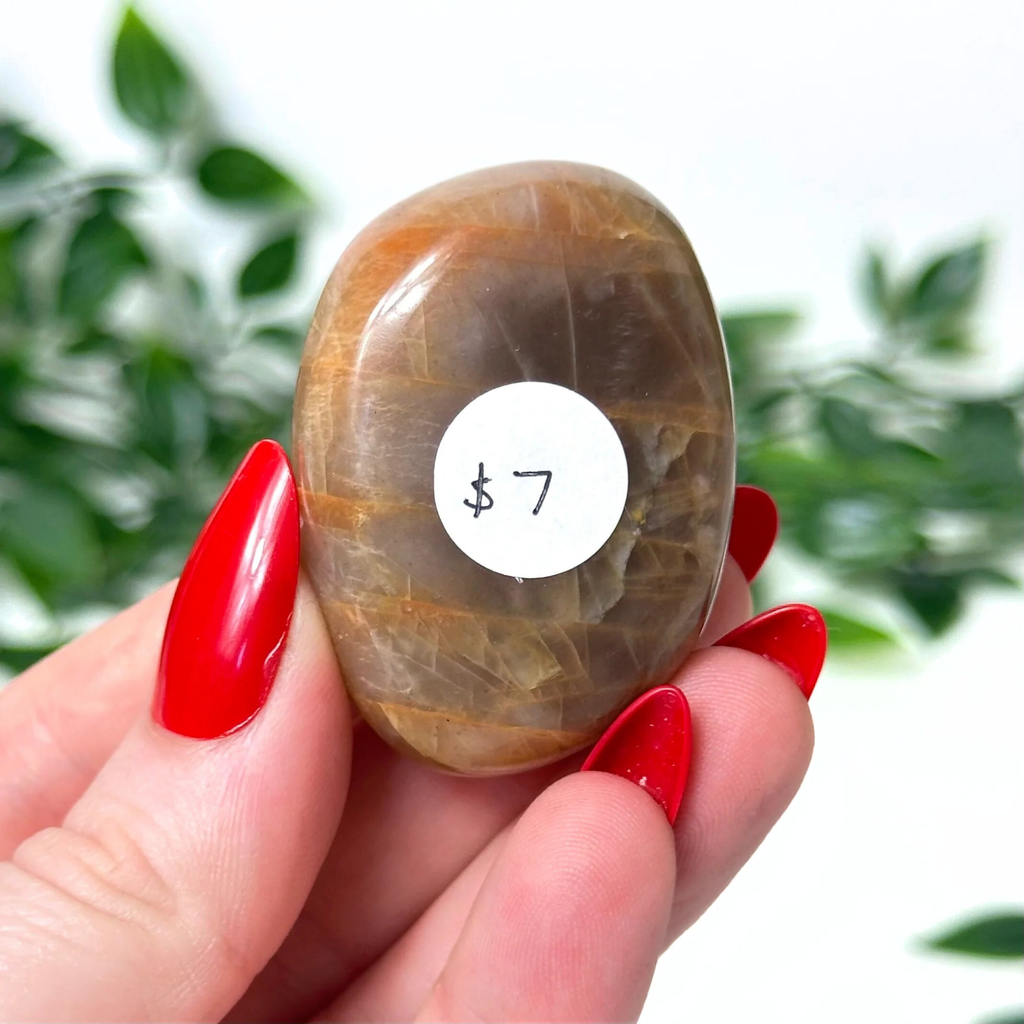 Hand holding a moonstone crystal against a blurred green background