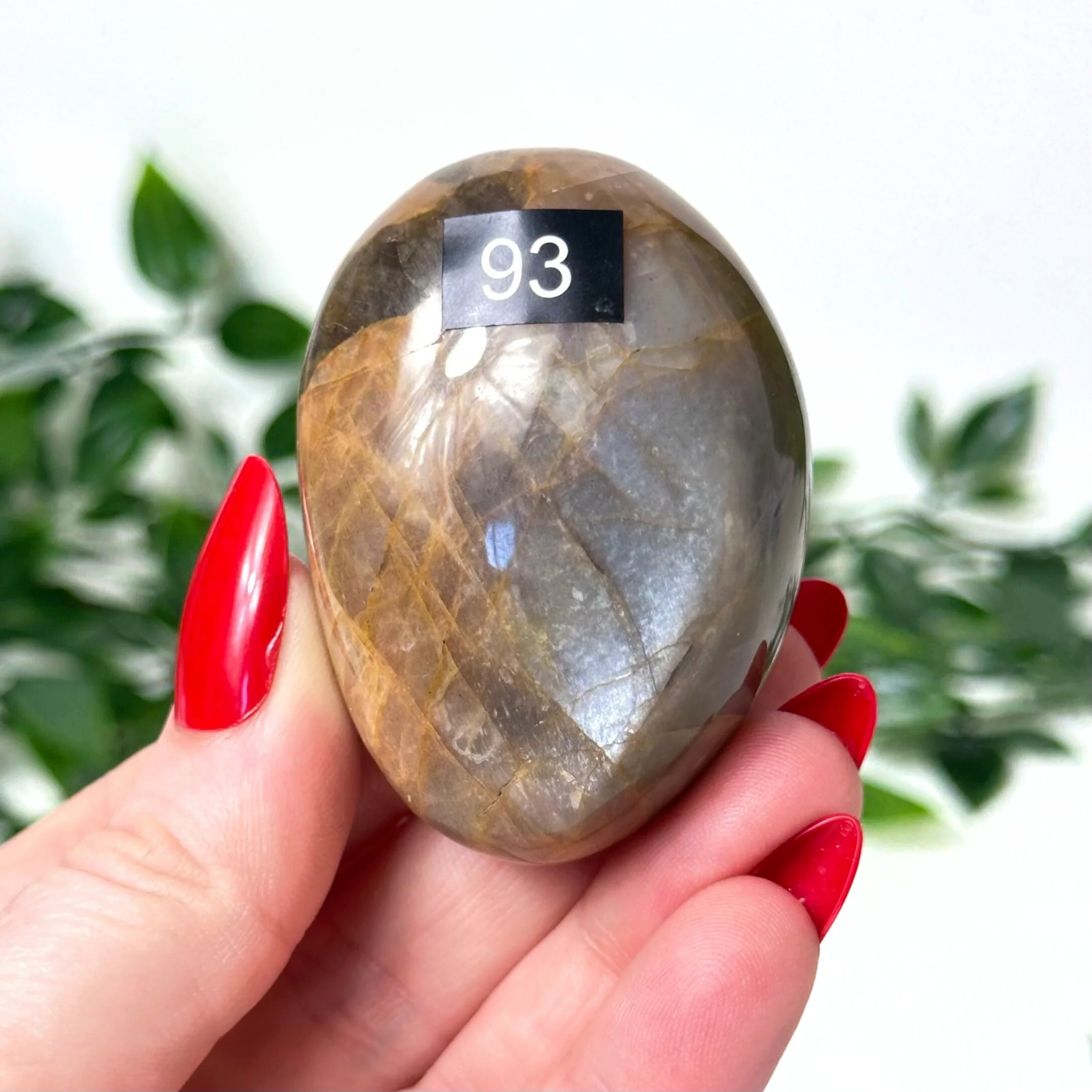 Hand holding a peach moonstone crystal against a white leafy background