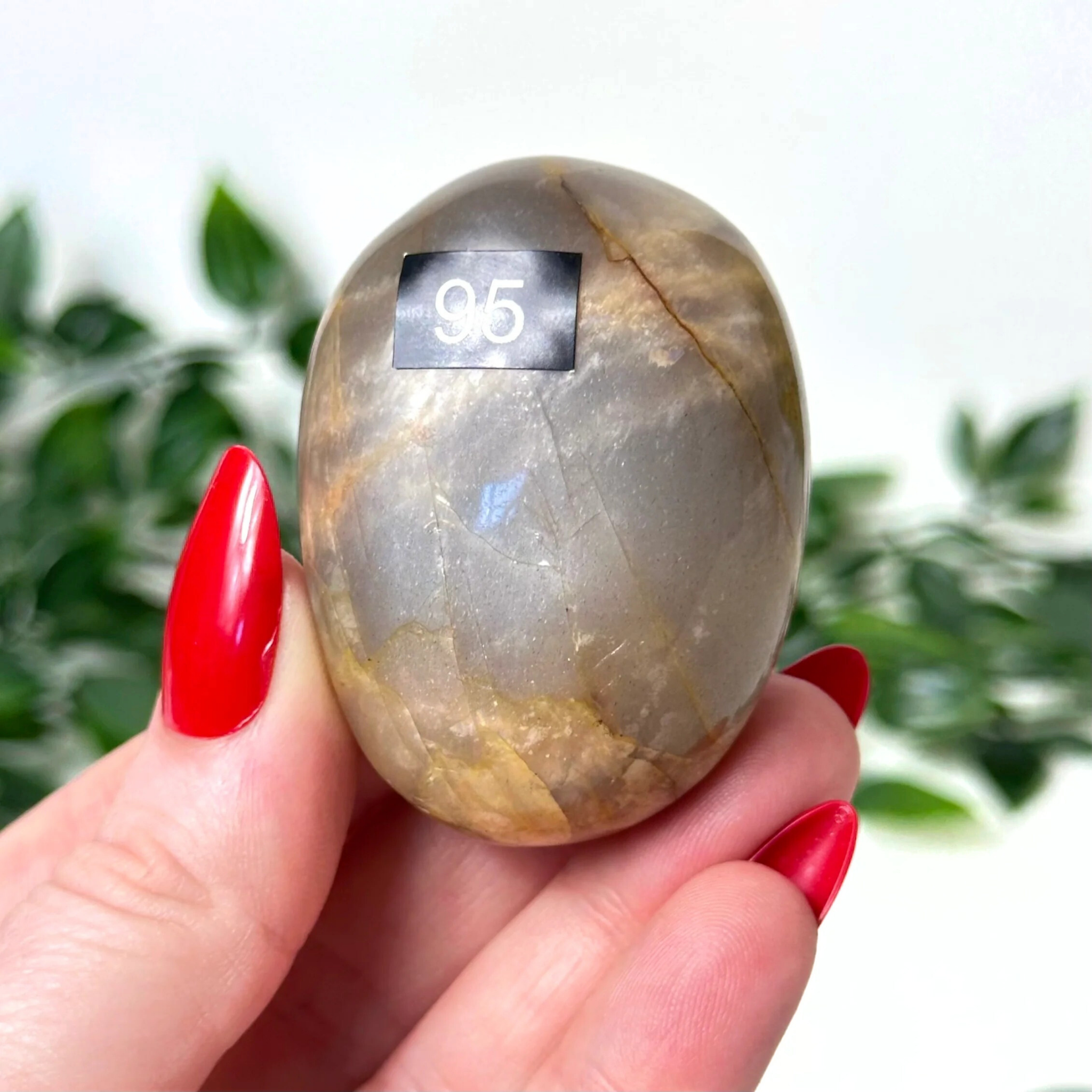 Hand holding a moonstone crystal against a blurred green background