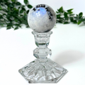 Moonstone crystal sphere on glass stand against a white background