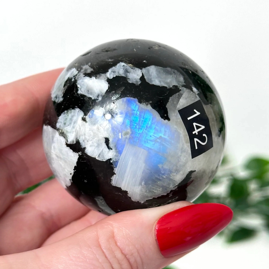 Hand holding a rainbow moonstone sphere against a white background