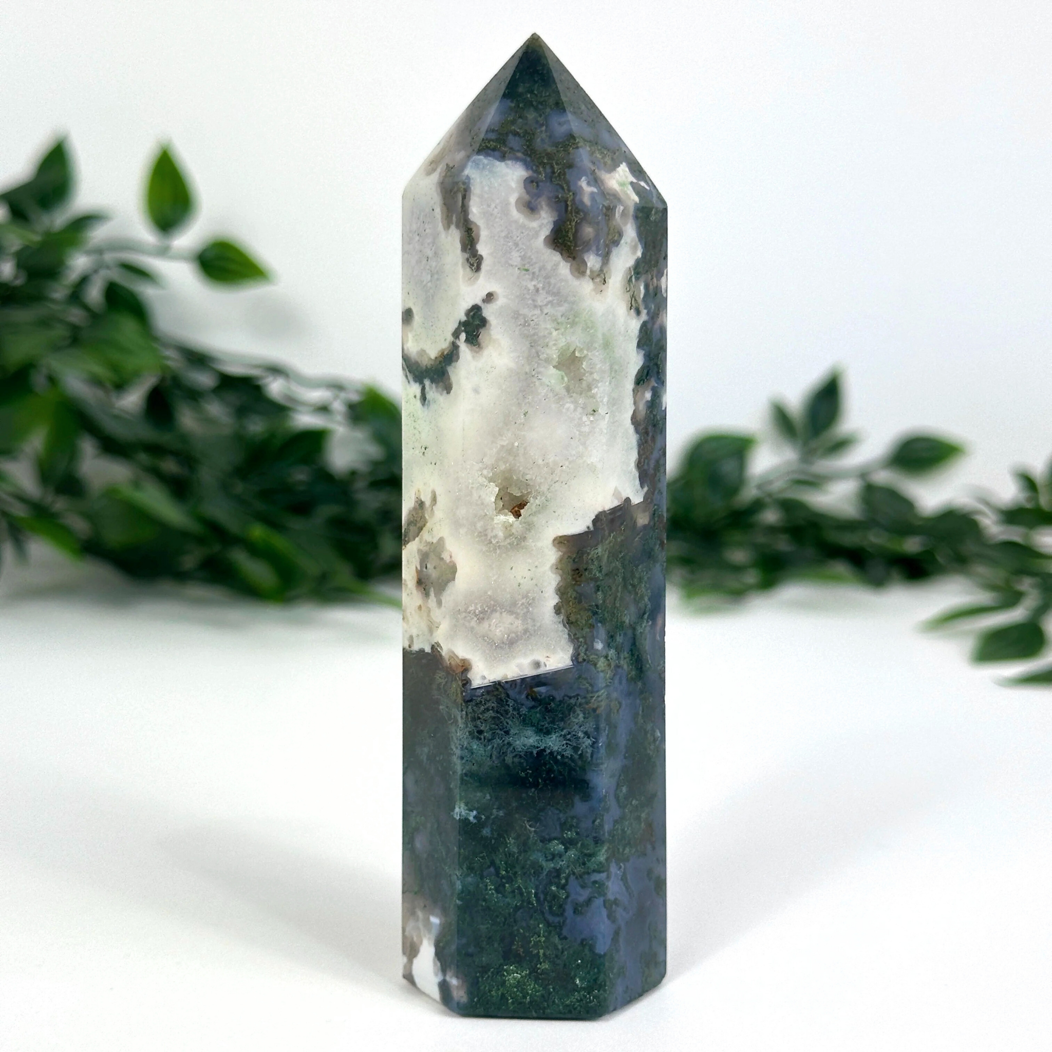 Moss agate crystal tower with green and white patterns on a white background with green leaves.