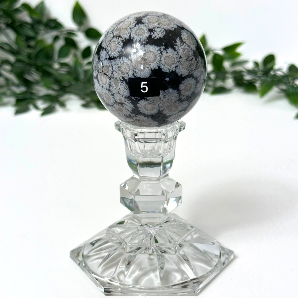 Snowflake obsidian crystal sphereon a stand against a white background