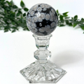 Snowflake obsidian crystal sphereon a stand against a white background