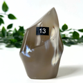 Polished orca agate crystal flame with a number 13 tag against a white background with green leaves.