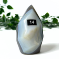 Polished orca agate flame with a number 14 label against a blurred green leafy background