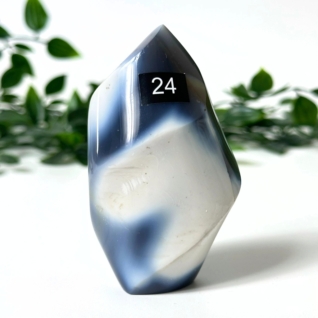Orca agate crystal flame with '24' on a white surface with green foliage in the background