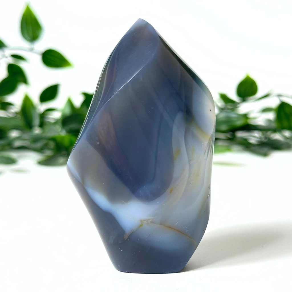 Grey orca agate crystal flame with a natural pattern on a white background with green leaves.