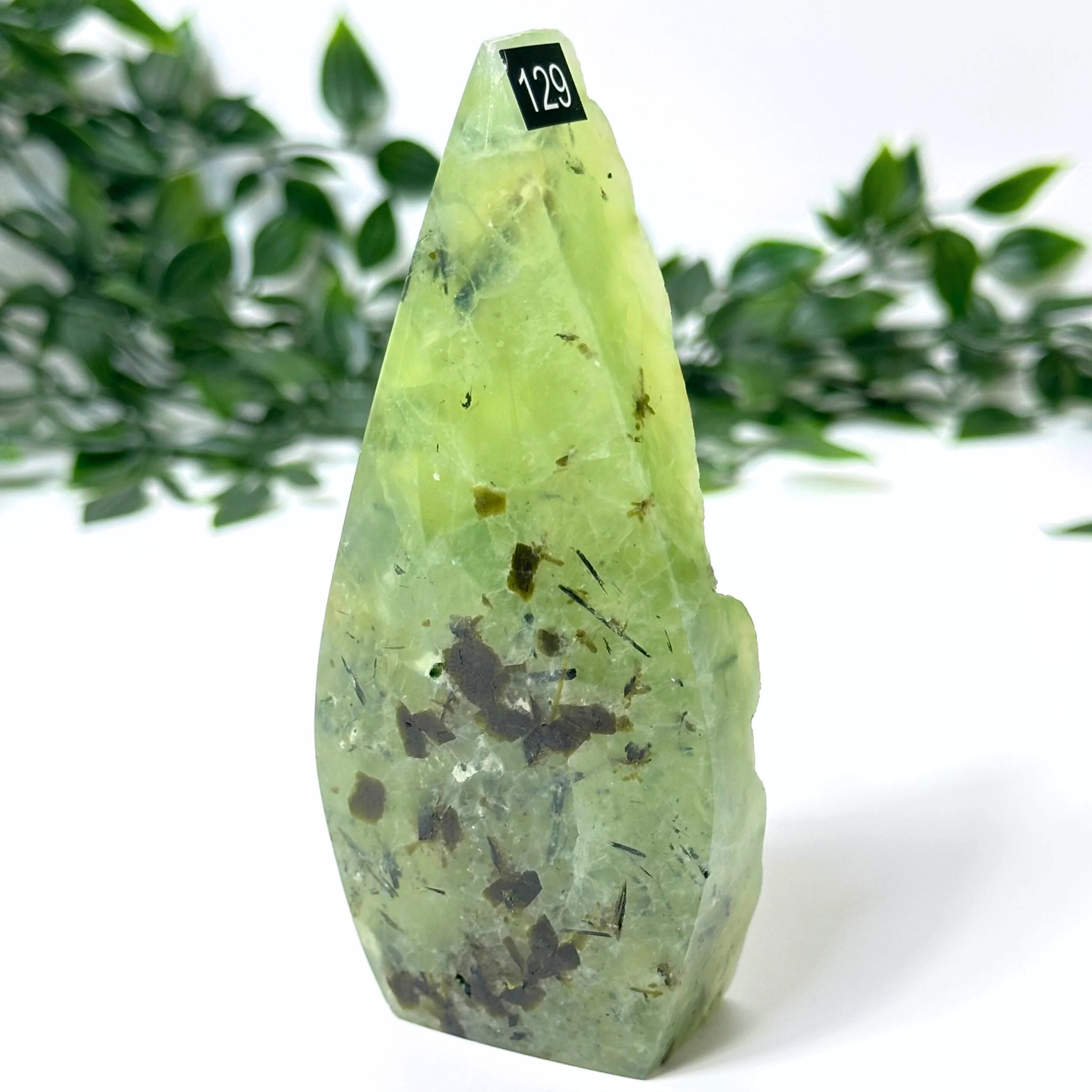 Prehnite crystal flame with black spots on a white background