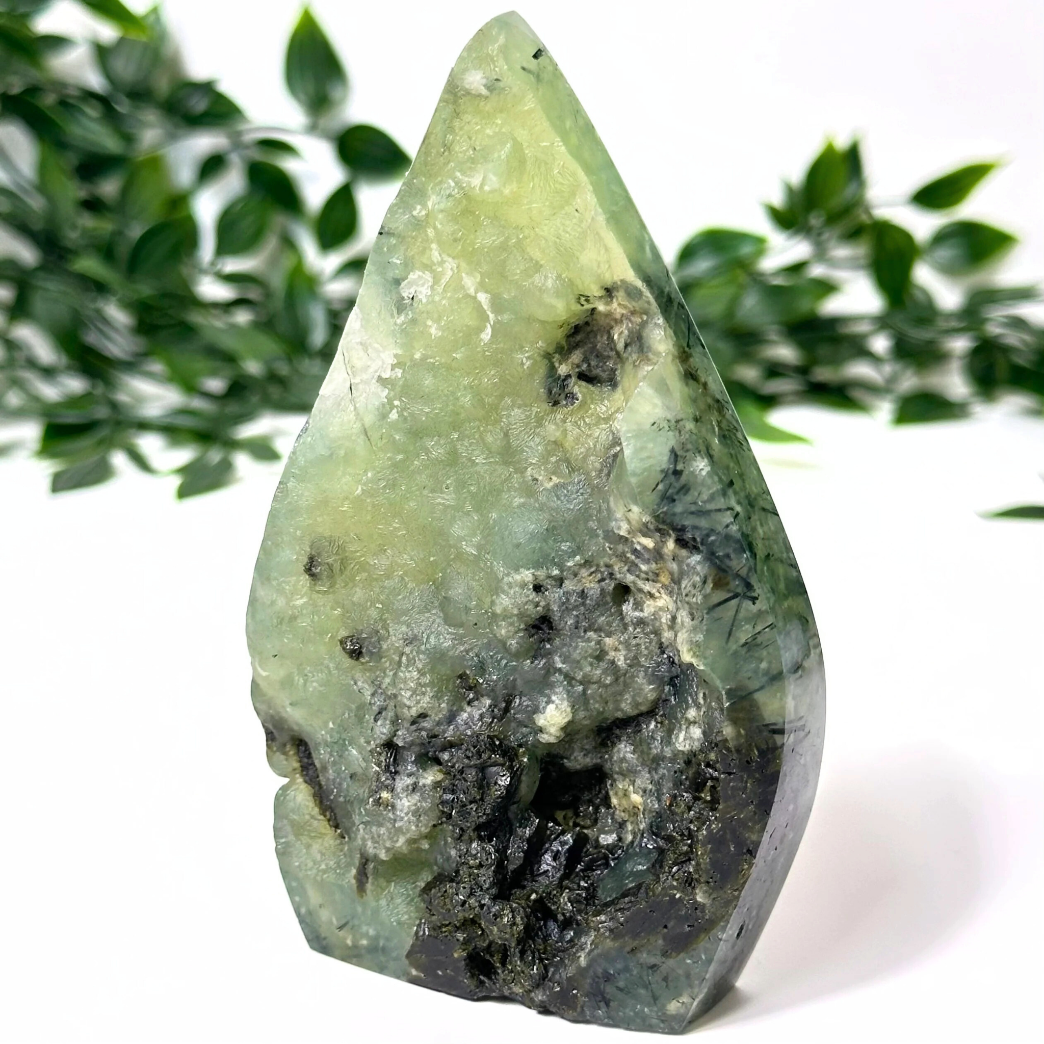 Prehnite crystal flame with black inclusions on a white background