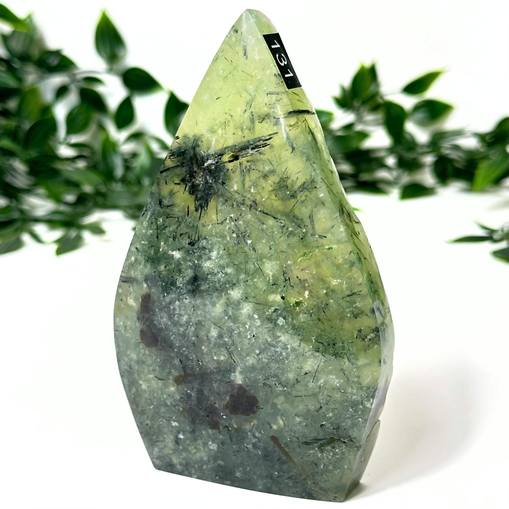 Prehnite crystal flame with black inclusions on a white background