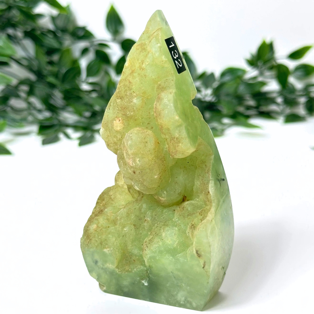 Prehnite crystal flame with a blurred green leafy background