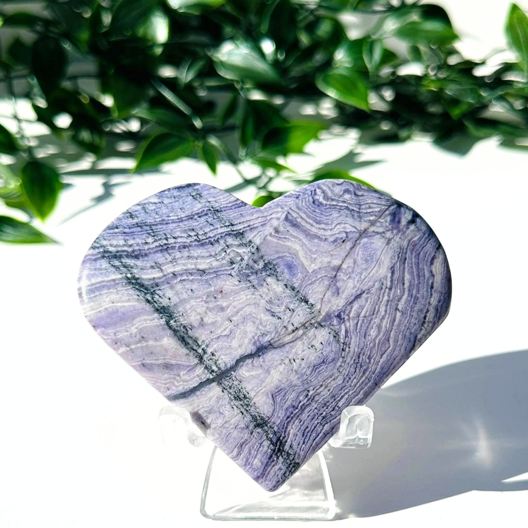Purple fluorite and white chalcedony crystal heart on stand with a white leafy background