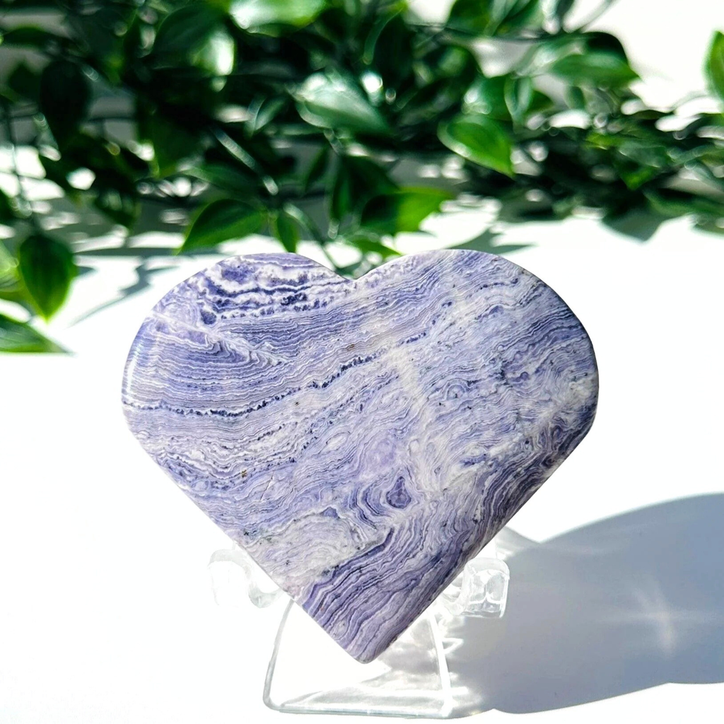 Purple fluorite and white chalcedony crystal heart on stand with a white leafy background