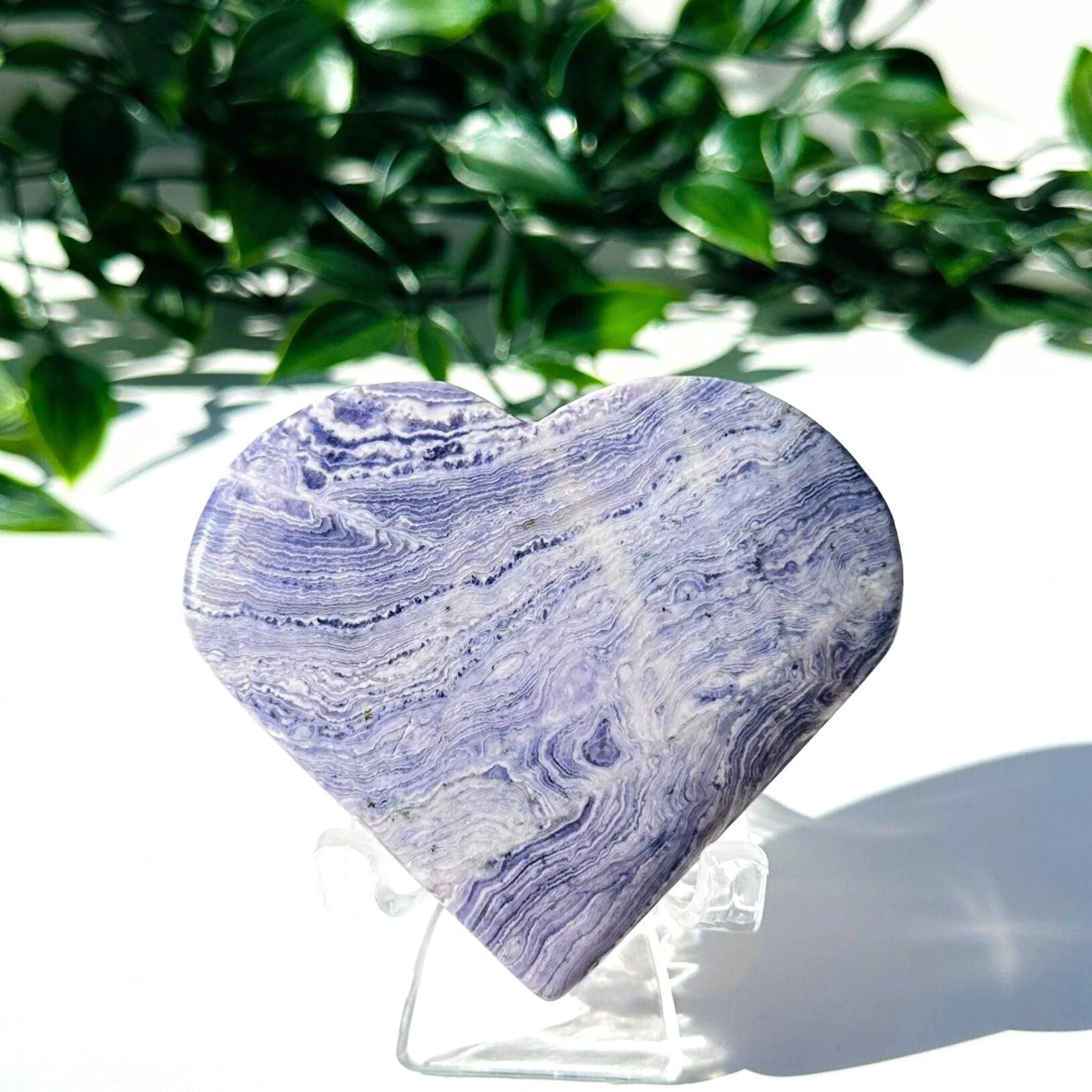 Purple fluorite and white chalcedony crystal heart on stand with a white leafy background