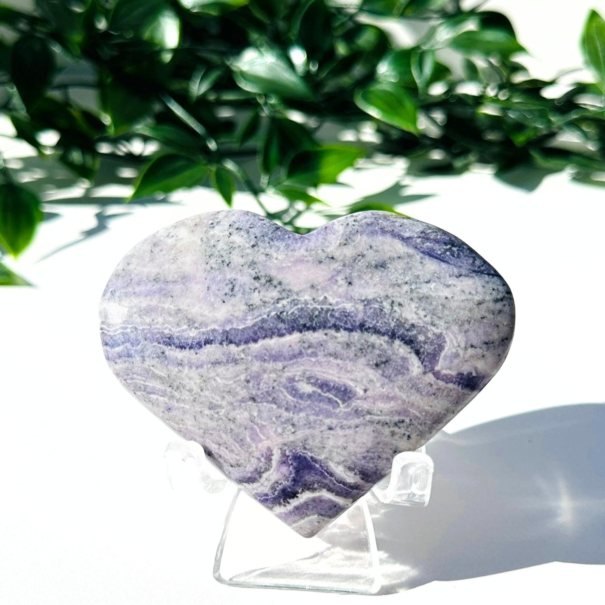 Purple fluorite and white chalcedony crystal heart on stand with a white leafy background