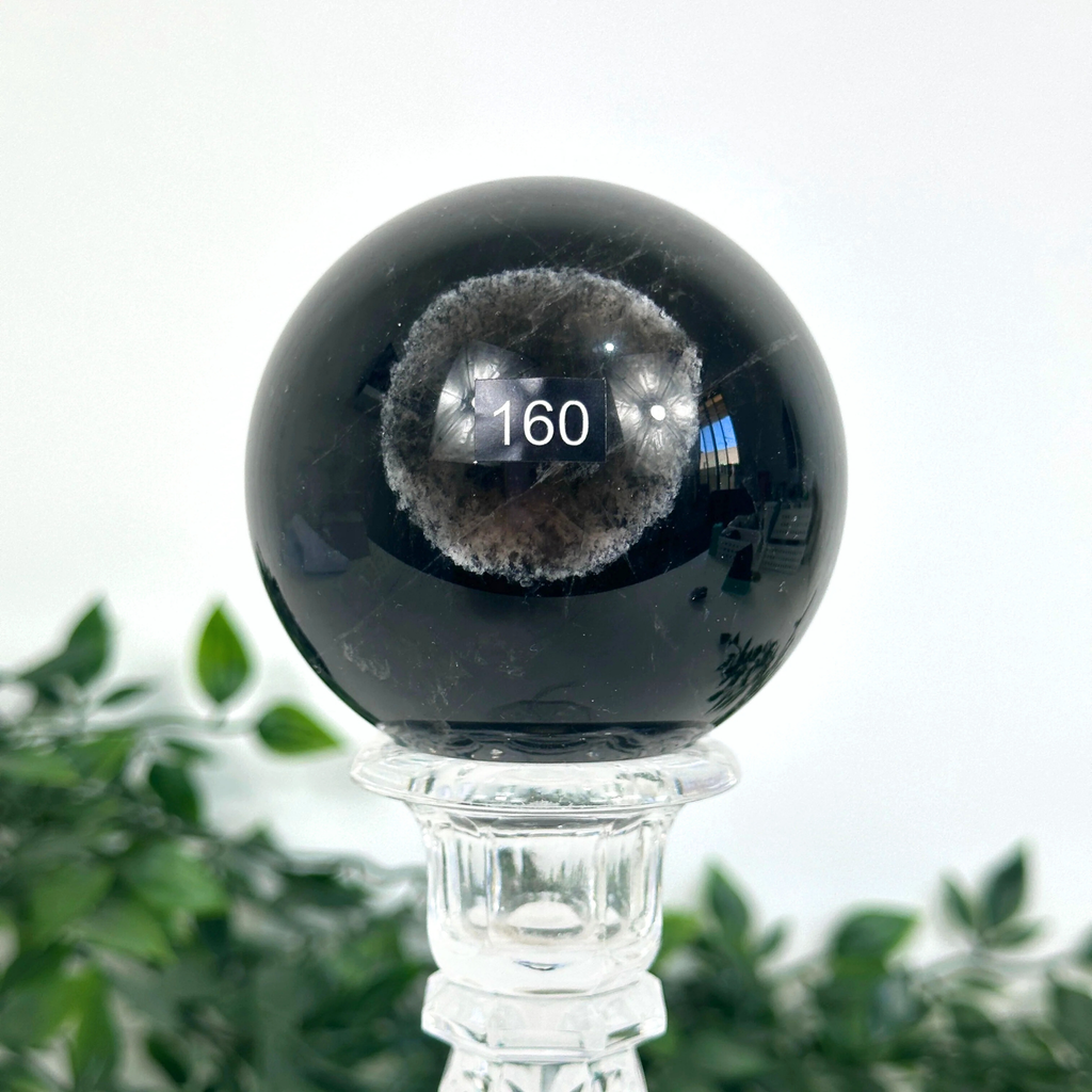 Smoky quartz crystal ball on a clear stand with a blurred green plant background