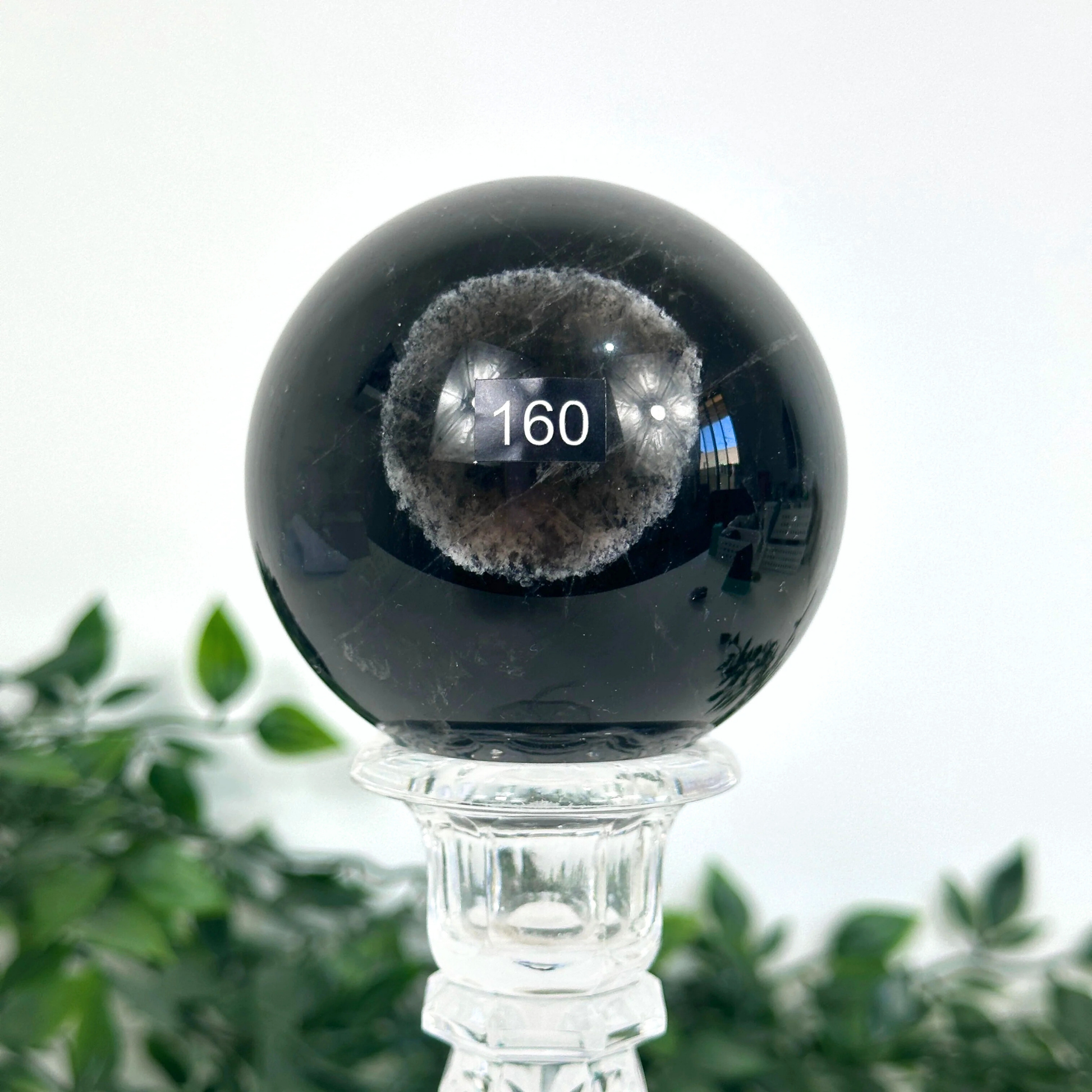 Smoky quartz crystal ball on a clear stand with a blurred green plant background