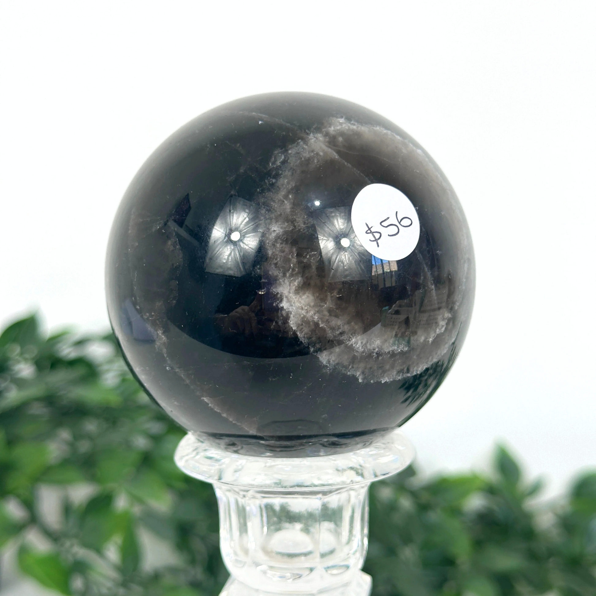 Smoky quartz crystal ball on a stand with a blurred green plant background