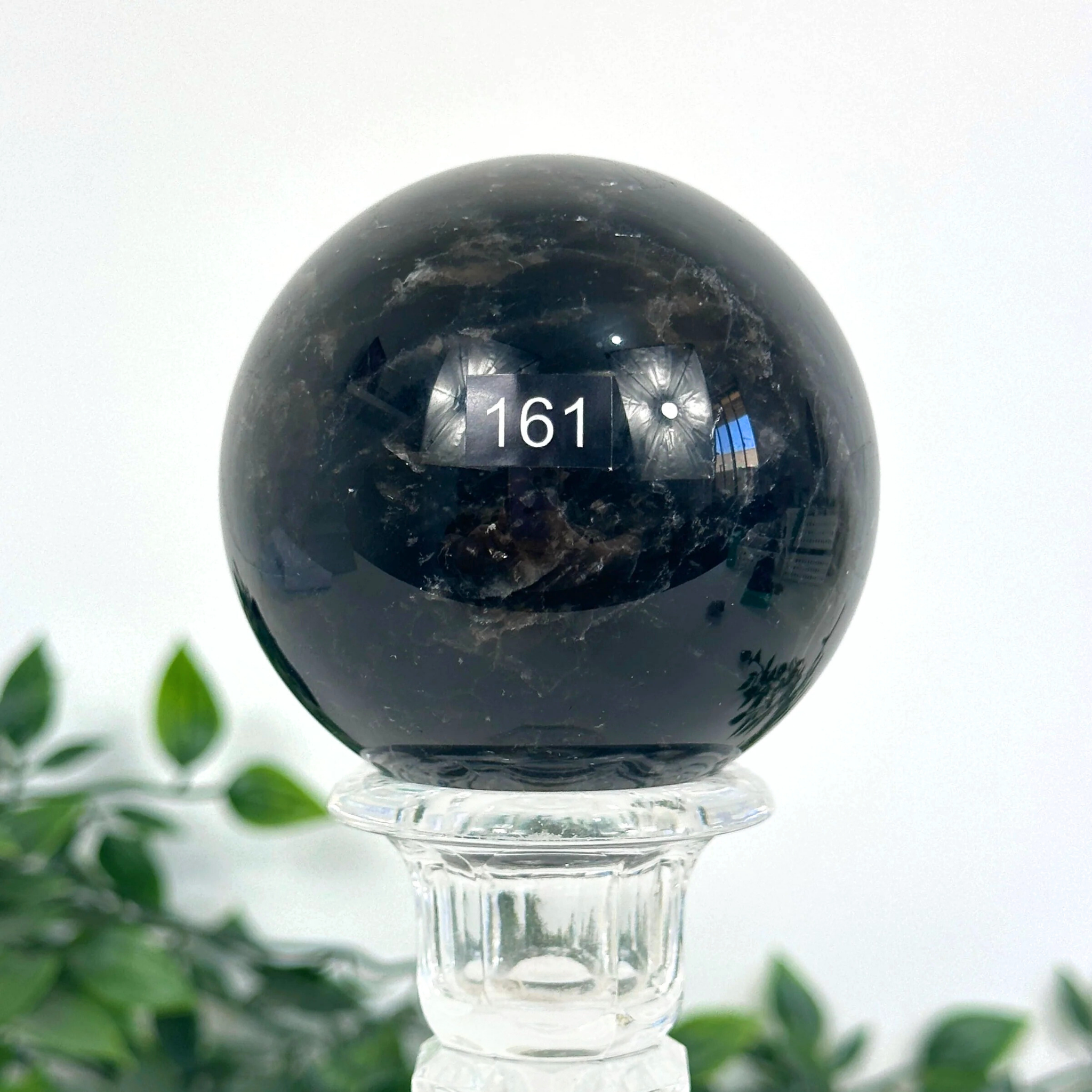 Smoky quartz crystal ball on a stand with a blurred green plant background