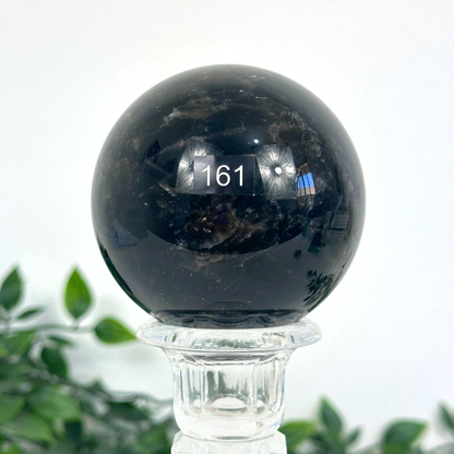 Smoky quartz crystal ball on a stand with a blurred green plant background