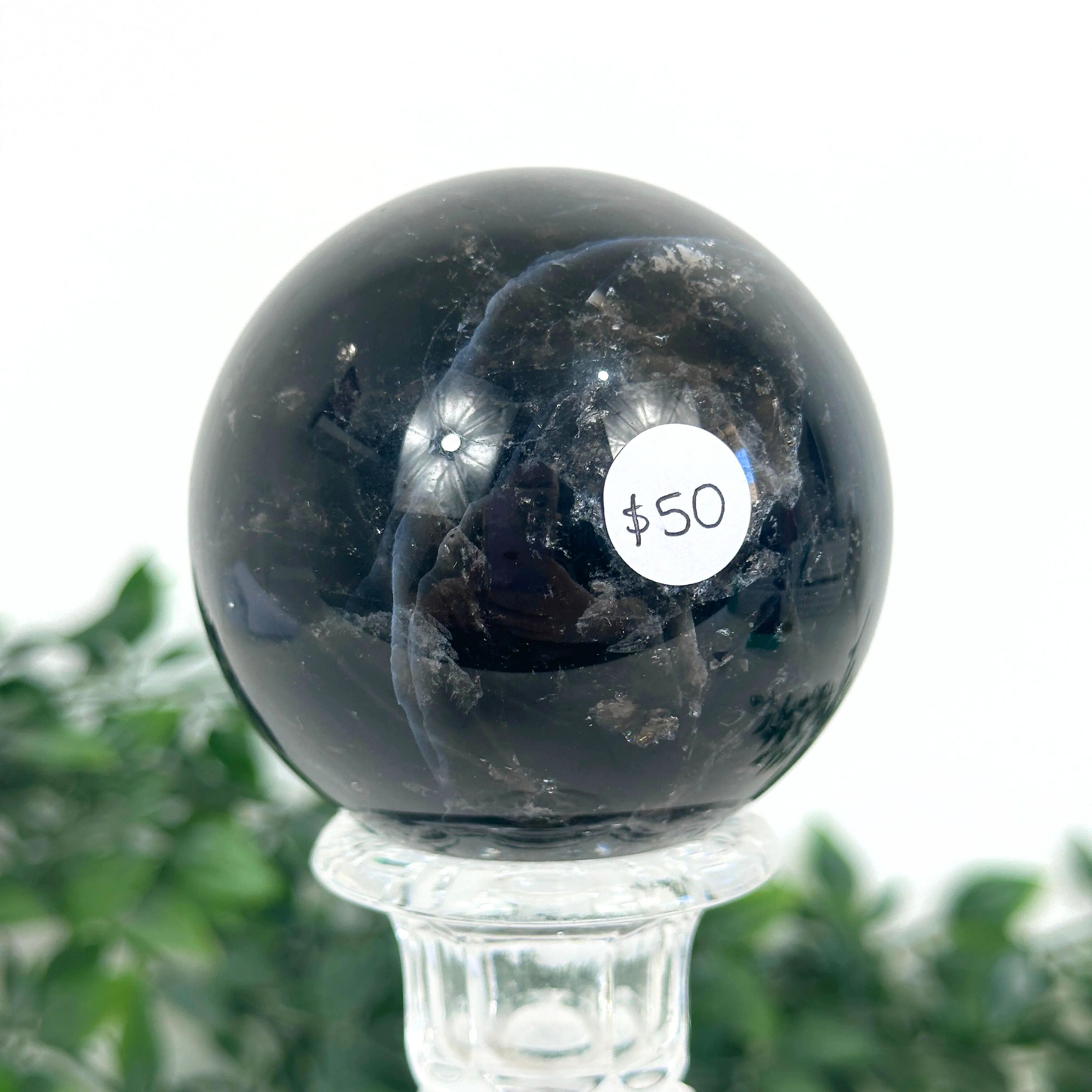 Smoky quartz crystal ball with a $50 label on a clear stand against a white background