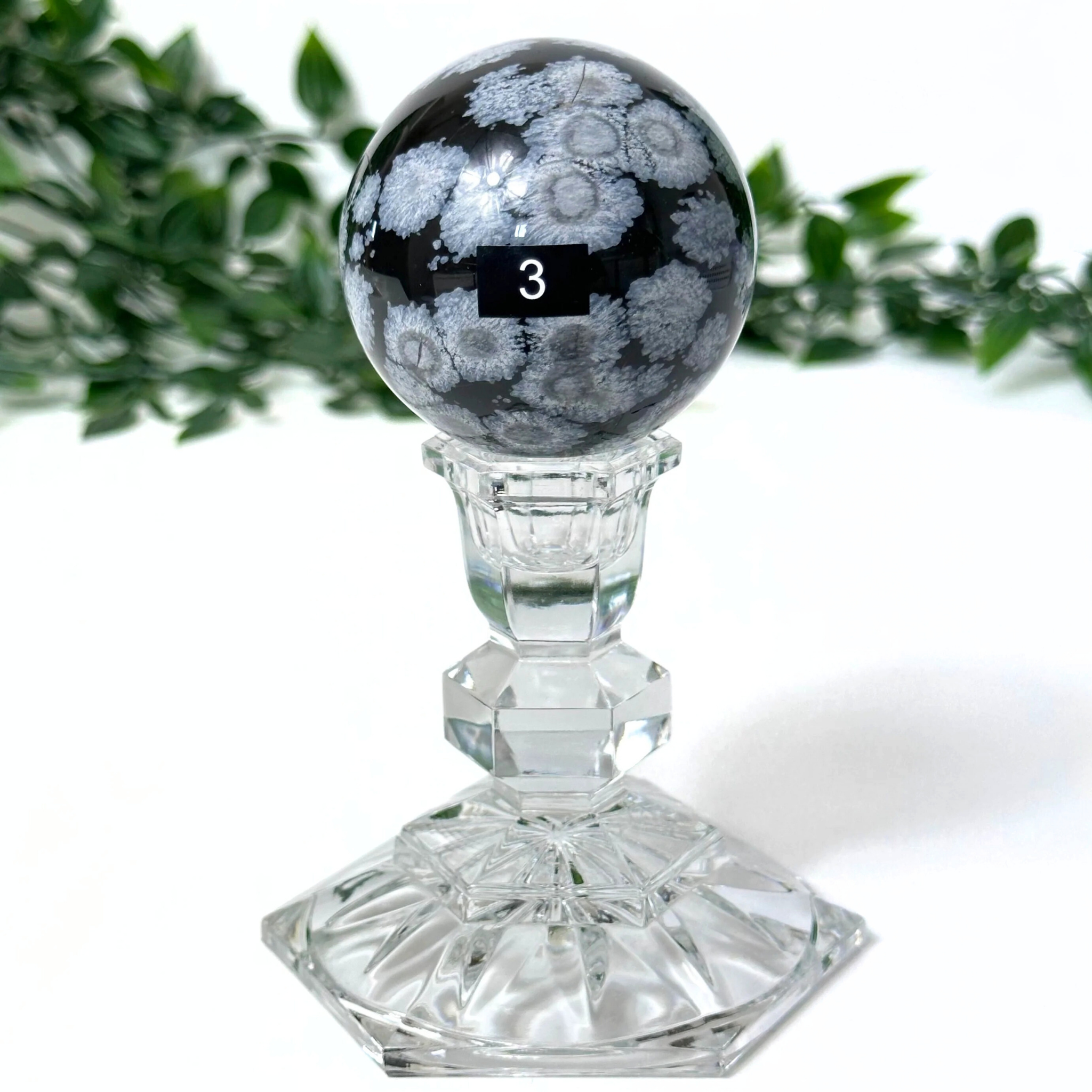 Snowflake obsidian crystal sphere on clear stand on a white background