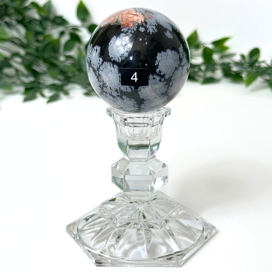 Snowflake obsidian crystal sphere on a clear pedestal against a white background.