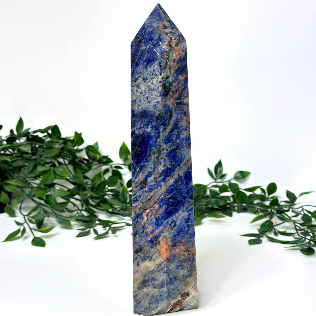 Extra large sodalite crystal tower with green foliage on a white background