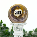 Mookaite crystal sphere on a clear stand with a blurred green background