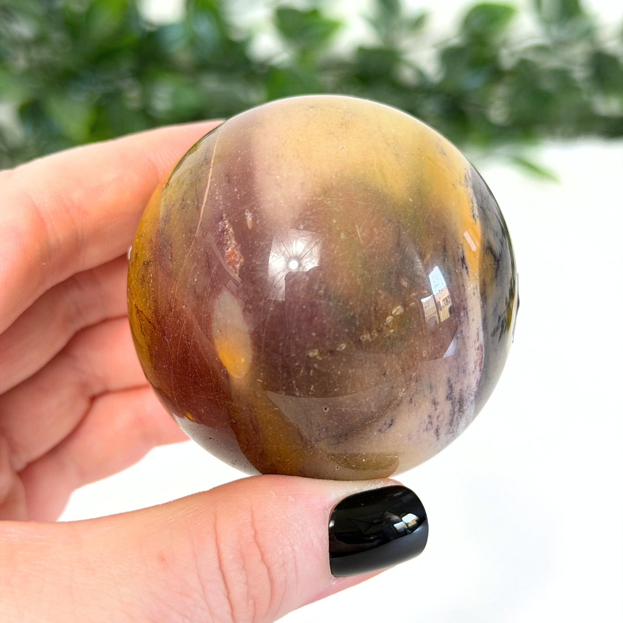 Hand holding a mookaite crystal sphere with a blurred green background