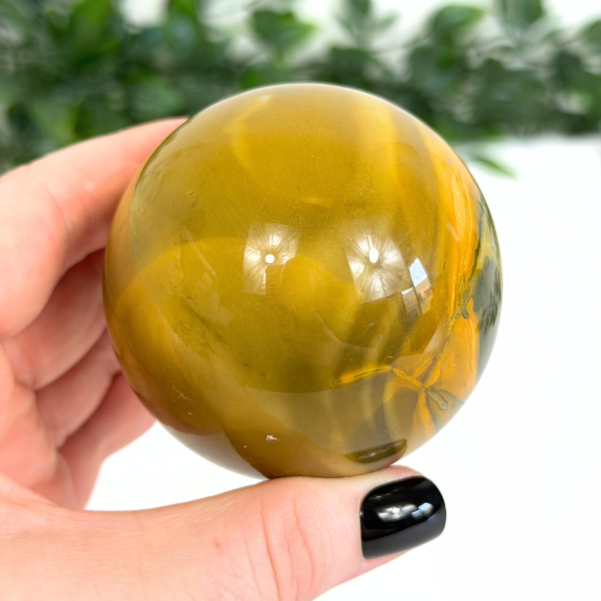 Hand holding a yellow mookaite crystal sphere with a blurred green background
