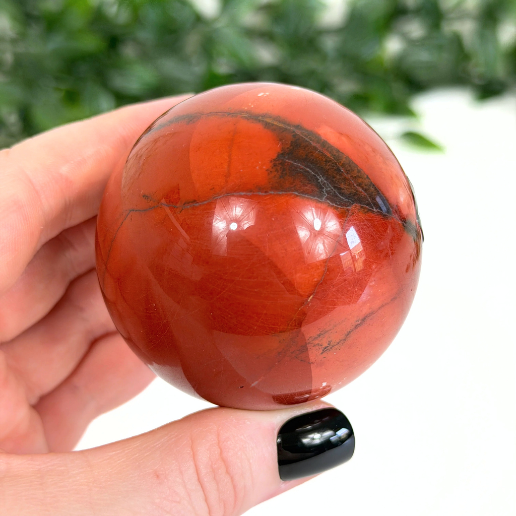 Hand holding a red mookaite sphere with a blurred green background
