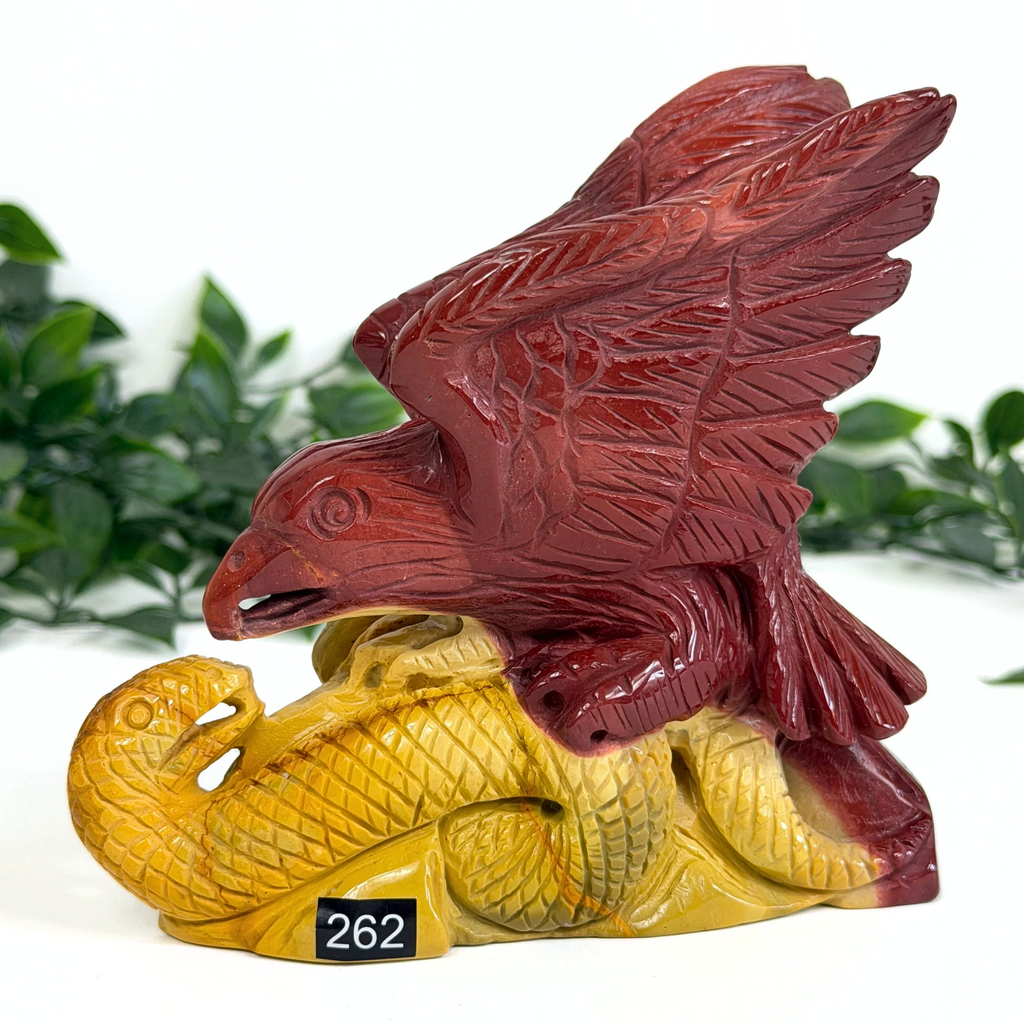 Decorative mookaite crystal sculpture of an eagle on a snake with a blurred green background