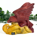 Decorative mookaite crystal sculpture of an eagle on a snake with a blurred green background