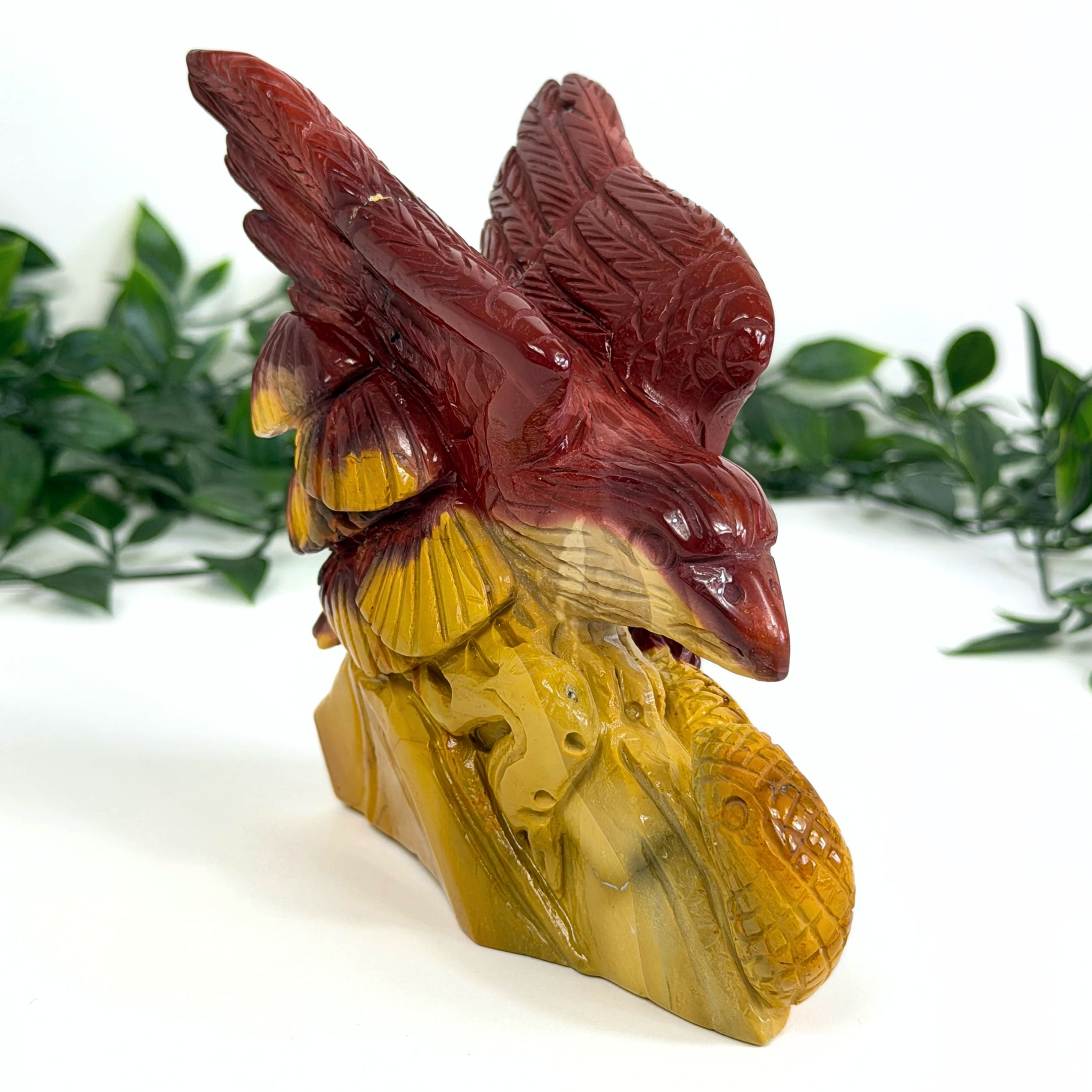 Carved mookaite sculpture of a eagle and snake with red and yellow colors on a white background
