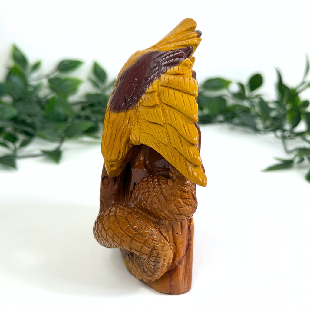 Crystal mookaite carved eagle and snake figure with green leaves in the background