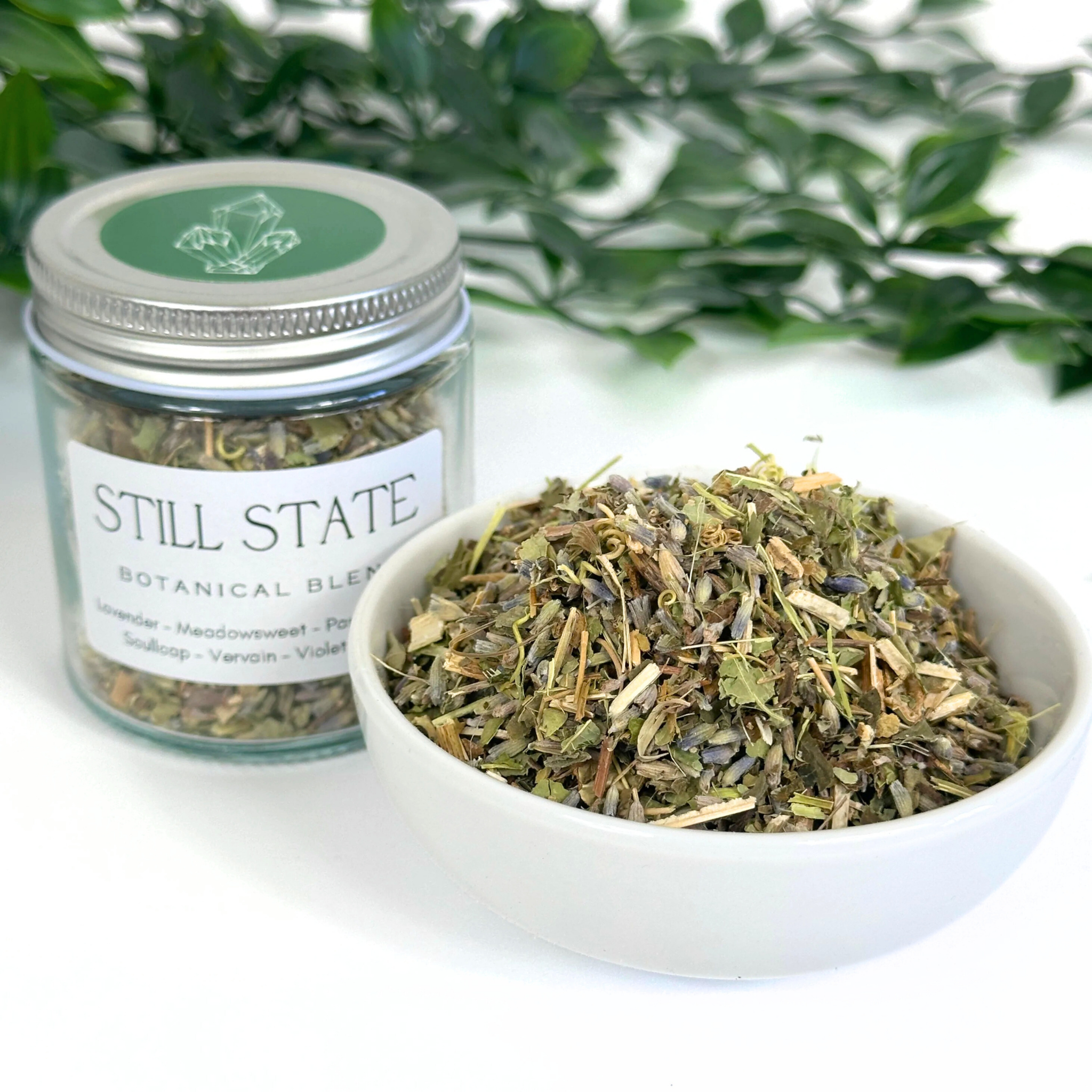 Jar and bowl of 'Still State' botanical blend with greenery in the background