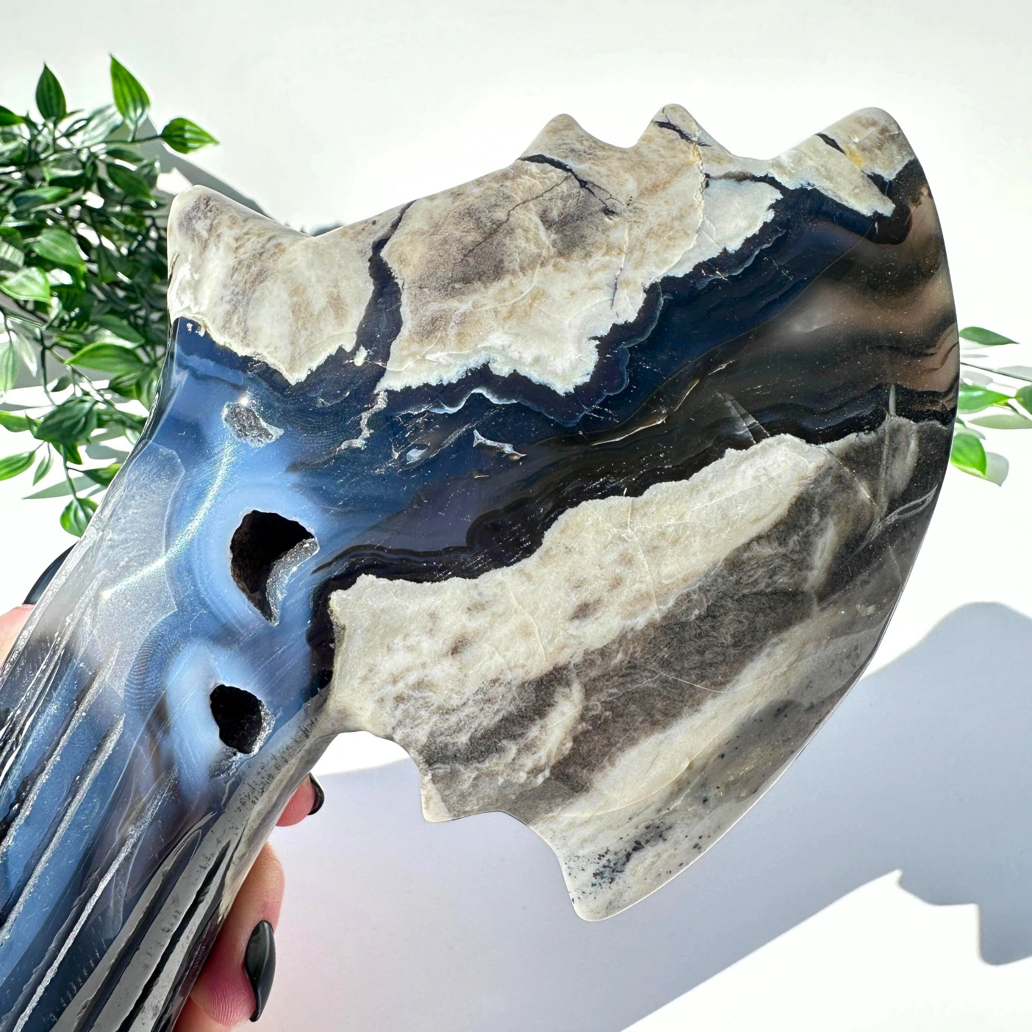 Hand holding a volcanic agate crystal axe against a white background