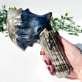 Hand holding a volcanic agate crystal axe with a natural pattern against a blurred green plant background