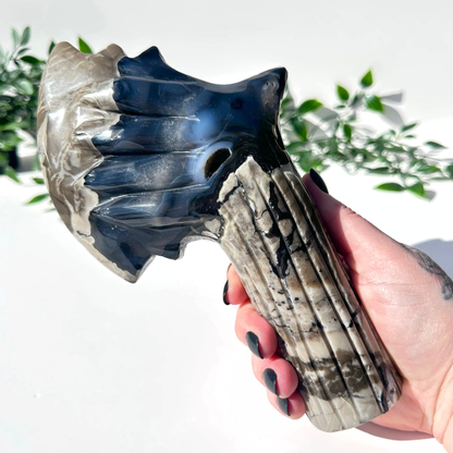 Hand holding a volcanic agate crystal axe with a natural pattern against a blurred green plant background