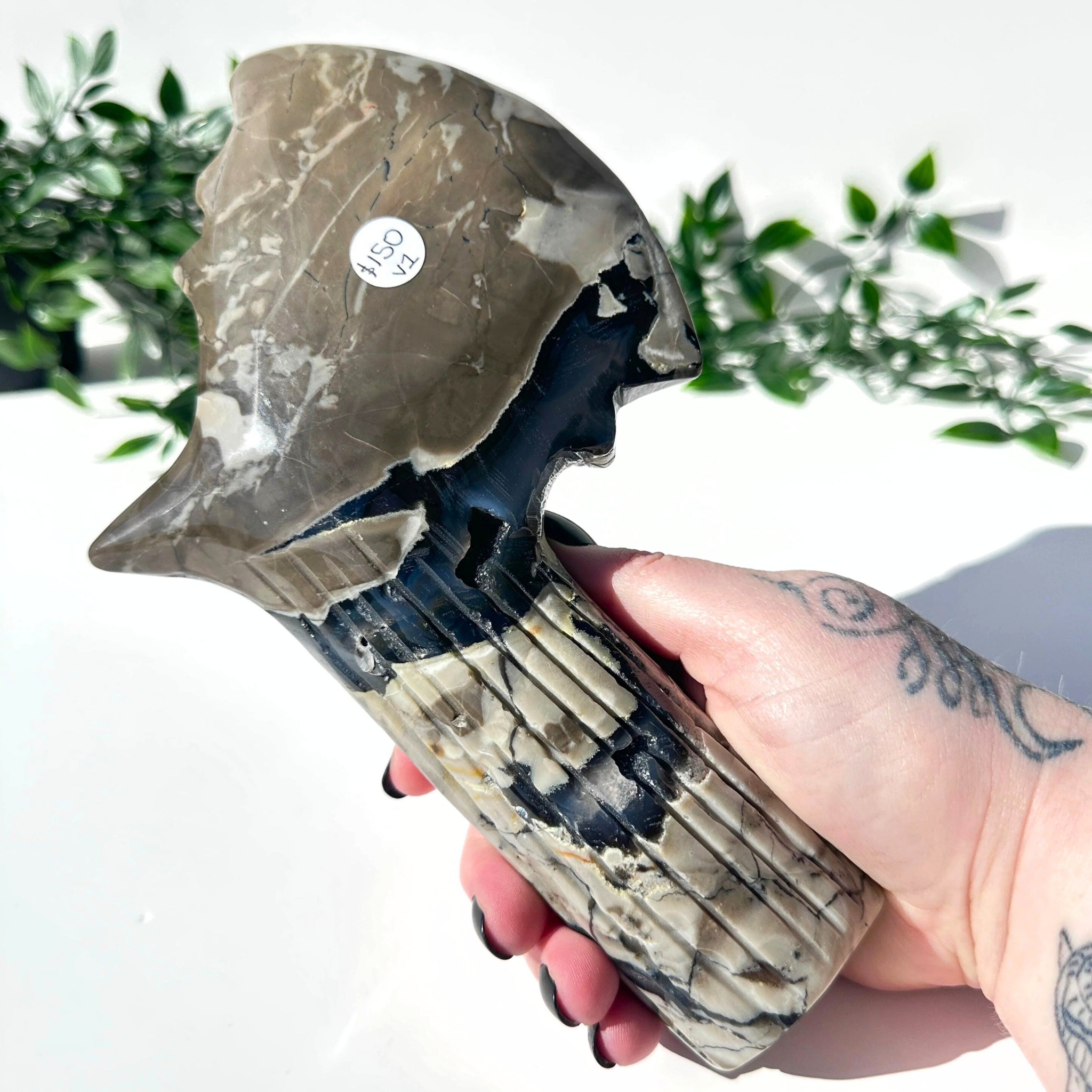 Hand holding a volcanic agate crystal axe with a natural pattern against a blurred green plant background