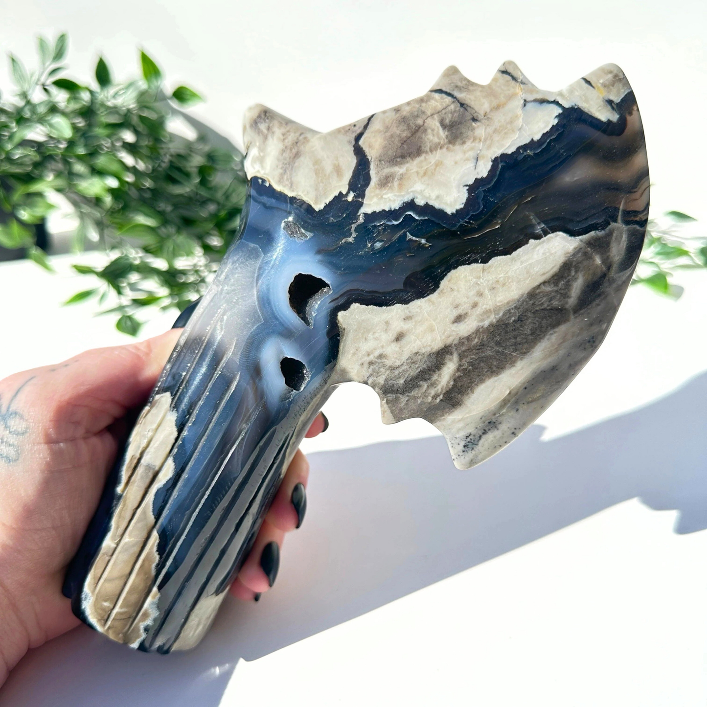 Hand holding a volcanic agate crystal axe against a white background